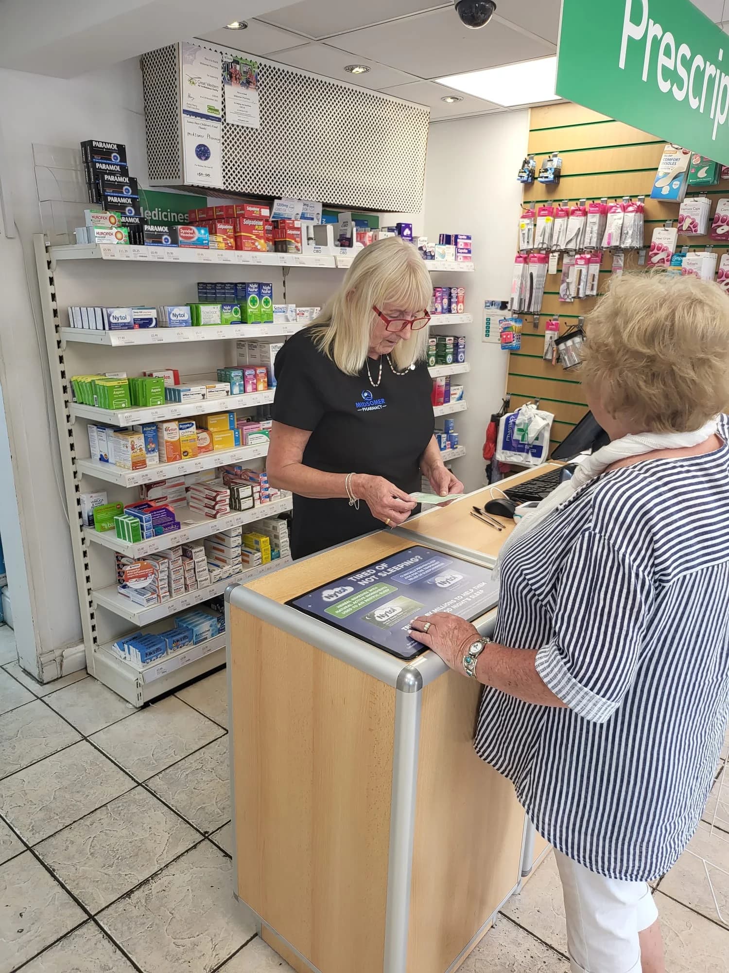 Pharmacist serving a customer at the counter of Midsomer Pharmacy